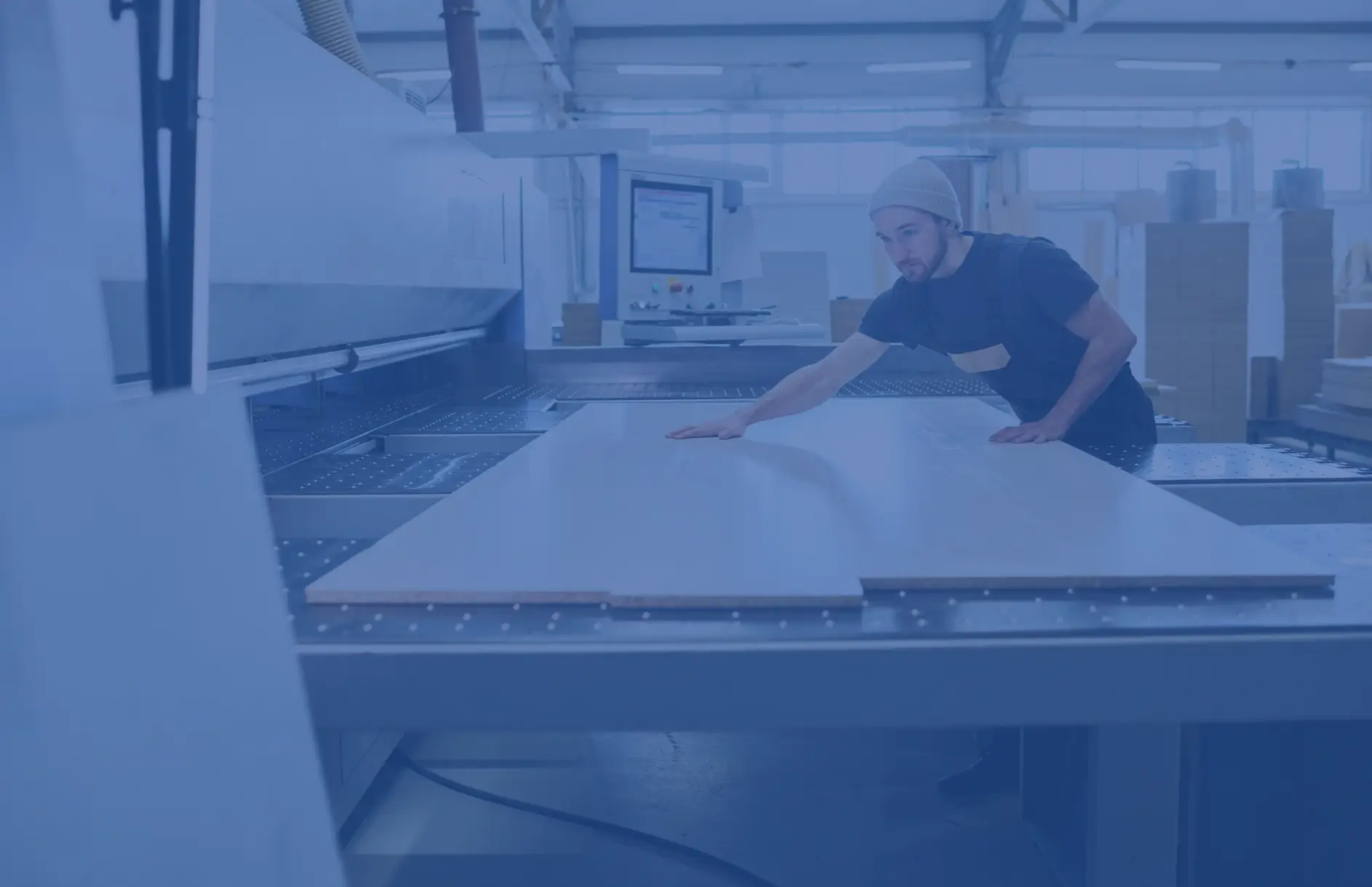 Worker putting material through a CNC machine making cabinets.